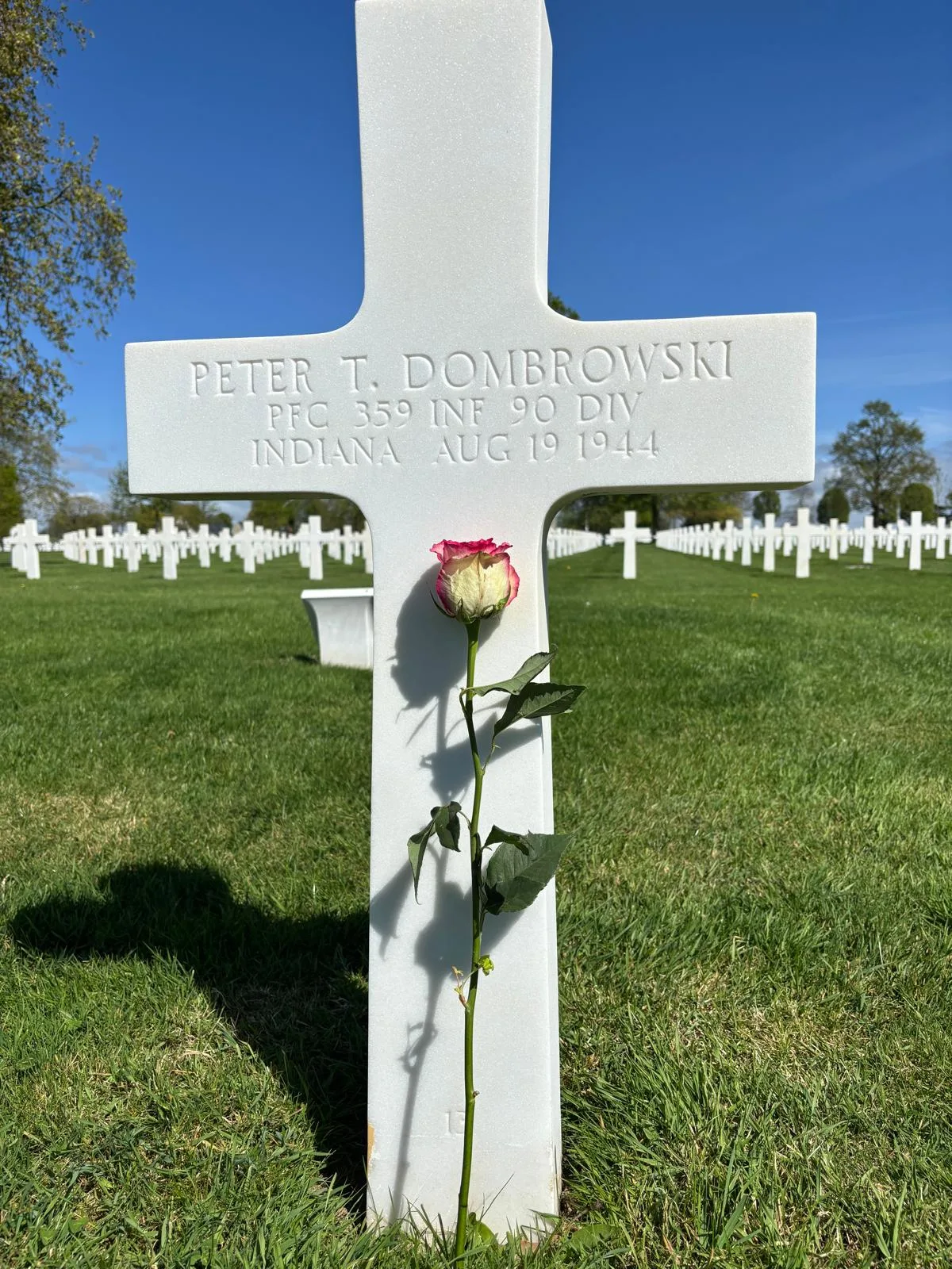 Babe Dombrowski's grave at the Brittany American Cemetery, with a pink and white rose against the marble cross