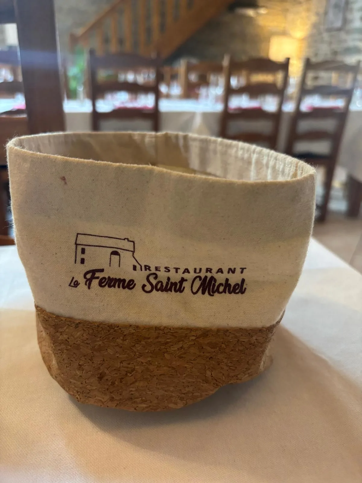 The cloth bread basket printed with the Ferme Saint-Michel logo on a white tablecloth