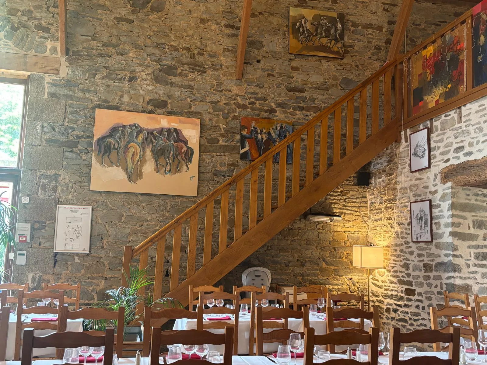 The stone dining room of La Ferme Saint-Michel with its wooden staircase, beamed ceiling and tables dressed in white linen